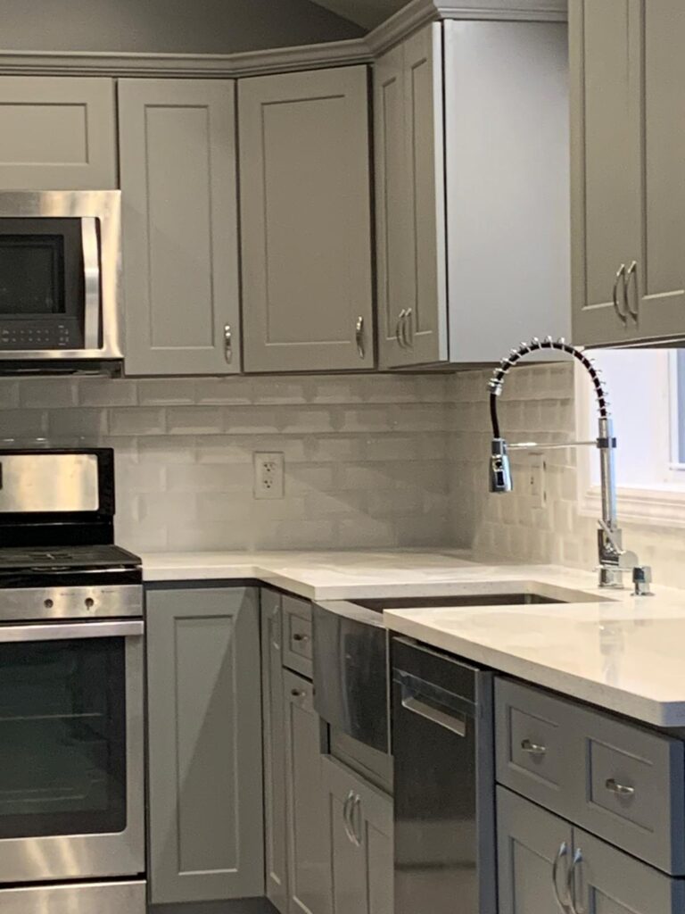 Modern white kitchen remodel with island, pendant lights, and stainless steel appliance